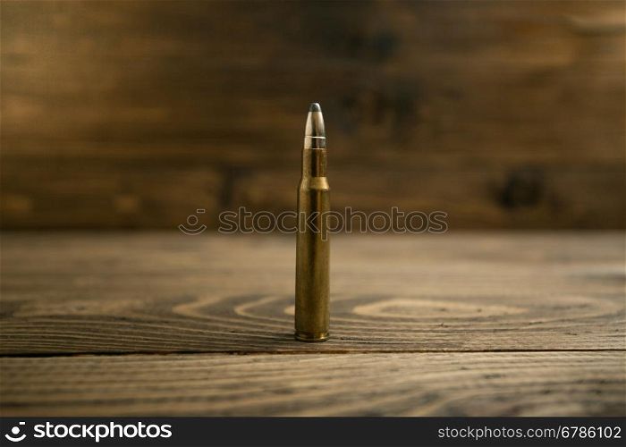 Closeup photo of riffle bullet on old wooden desk