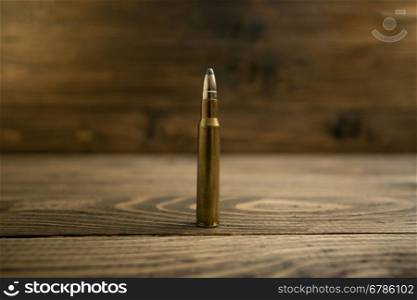 Closeup photo of riffle bullet on old wooden desk