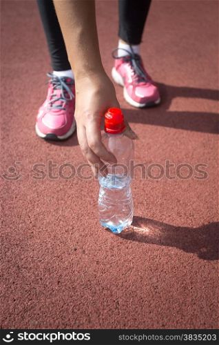 Closeup photo of sporty woman taking bottle of water from running track