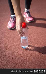 Closeup photo of sporty woman taking bottle of water from running track
