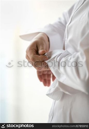 Closeup photo of stylish man in white shirt putting on cufflinks