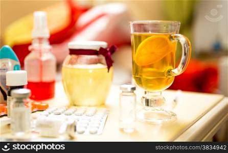 Closeup photo of tea and medicines on table next to bed