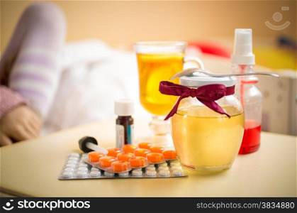 Closeup photo of tea, honey jar and pills lying on table at bedroom