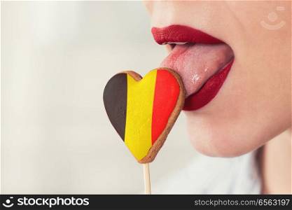 Closeup photo of the woman lips and cookie hearts with flag of Belgium. Lips and cookie with flag. Lips and cookie with flag