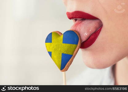 Closeup photo of the woman lips and cookie hearts with flag of Sweden. Lips and cookie with flag. Lips and cookie with flag