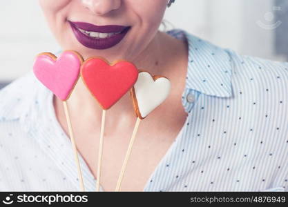 Closeup photo of the woman lips and gingerbread hearts on a stick, concept of love or valentines das