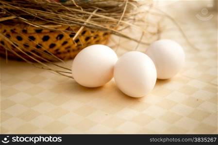 Closeup photo of three white eggs lying on table next to basket