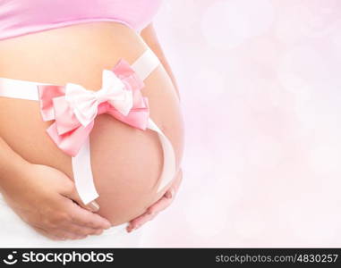 Closeup photo of tummy of pregnant woman with pink ribbon bow isolated on blur background, body part, best gift for young family, it's a girl concept