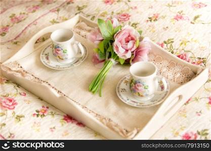 Closeup photo of vintage tray with flowers and teacups lying on bed