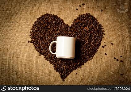 Closeup photo of white mug in middle of heart made of coffee beans
