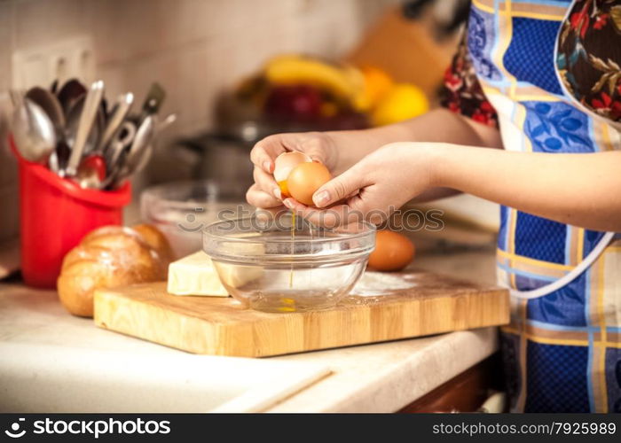 Closeup photo of woman breaking egg in glass bowl