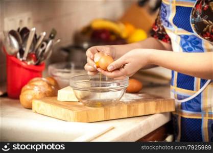 Closeup photo of woman breaking egg in glass bowl