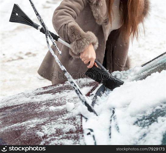 Closeup photo of woman cleaning snow from car hood with brush