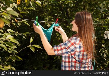 Closeup photo of woman hanging blue bikini on clothesline at garden