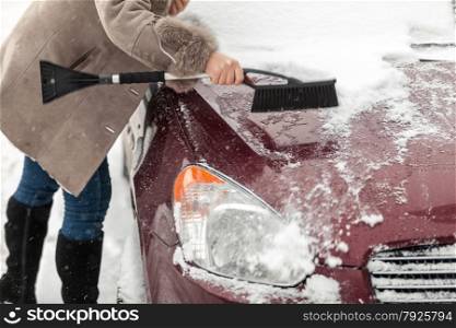 Closeup photo of woman holding brush and cleaning snow from car