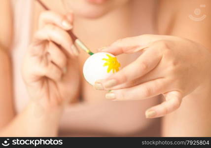 Closeup photo of woman holding white egg and painting it with yellow color