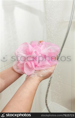 Closeup photo of woman lathering pink sponge at shower