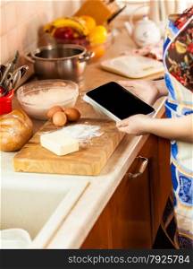 Closeup photo of woman looking recipe on tablet while making dough