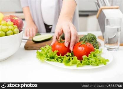 Closeup photo of woman picking fresh tomato from table on kitchen