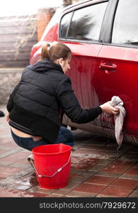 Closeup photo of woman sitting next to red car and washing door