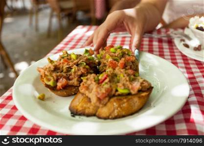 Closeup photo of woman taking bruschetta with tuna from plate at restaurant