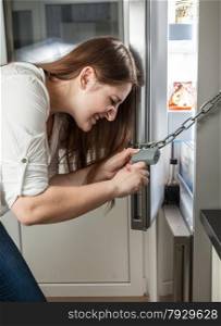 Closeup photo of woman trying to open lock hanging on fridge