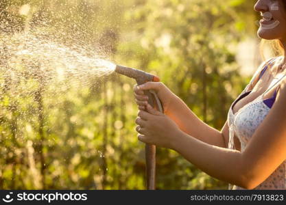 Closeup photo of woman watering garden with hosepipe at hot sunny day