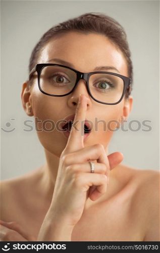Closeup photo of woman wearing glasses and making a hush gesture