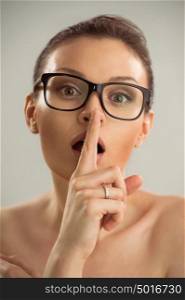Closeup photo of woman wearing glasses and making a hush gesture
