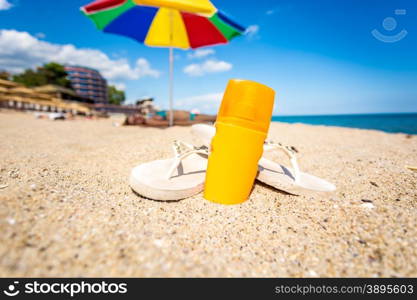 Closeup photo of yellow suntan lotion and flip flops lying on sandy beach