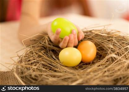 Closeup photo of young girl taking green Easter egg from the nest