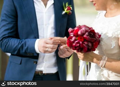 Closeup photo of young groom putting wedding ring on bride&rsquo;s finger