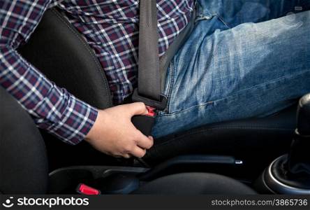 Closeup photo of young man seating on drivers seat and fastening belt