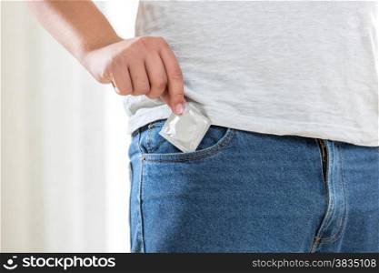 Closeup photo of young man taking condom out of pocket in jeans