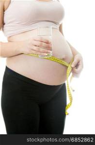 Closeup photo of young pregnant woman holding glass of water and measuring belly.