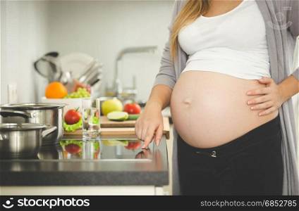 Closeup photo of young pregnant woman turning on electric stove