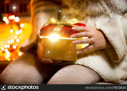 Closeup photo of young woman opening gift box with light coming out of it