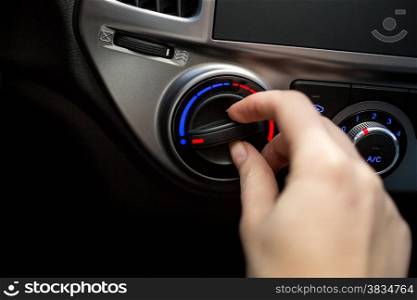 Closeup photo of young woman turning car air conditioner switch
