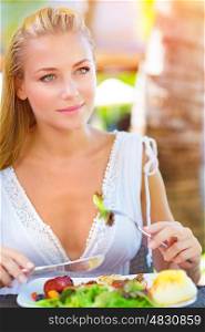 Closeup portrait cute blond girl sitting in outdoors restaurant and having breakfast, eating fresh vegetables salad, luxury healthy eating concept&#xA;