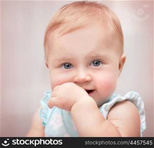 Closeup portrait of a beautiful little baby girl with hand in the mouth over pastel pink background, carefree childhood, precious innocent kid