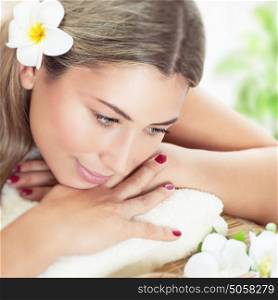 Closeup portrait of a beautiful woman at spa, nice female with fresh frangipani flower in hair lying down on massage table, pampering and relaxation in the beauty salon