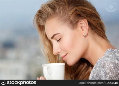 Closeup portrait of a beautiful woman with closed eyes enjoying aroma of morning coffee, taking breakfast in outdoor cafe
