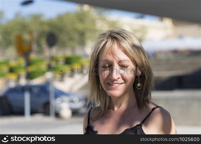Closeup portrait of a blonde woman eyes closed while smiling outdoors in a sunny day