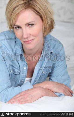 Closeup portrait of a blonde woman lying on a bed in a denim shirt
