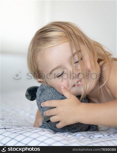 Closeup portrait of a cute baby boy having fun with soft toy doggy on the bed at home, happy carefree childhood