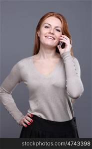 Closeup portrait of a cute young woman talking on mobile phone against grey background