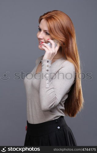 Closeup portrait of a cute young woman talking on mobile phone against grey background