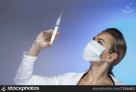 Closeup Portrait of a Doctor Wearing Mask with Syringe in Hand isolated on Blue Background. Beauty Treatment. Injection of Beauty. Women’s Beauty.. Doctor with a Syringe