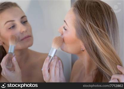 Closeup Portrait of a Gentle Blond Woman Doing Makeup near the Mirror. Applies Blush and Looks at her Reflection. Young Female.. Woman Doing Makeup