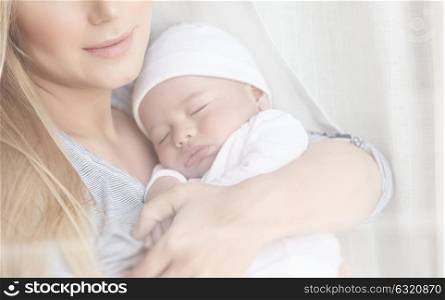Closeup portrait of a gentle mother holding in hands her newborn sleeping baby, happy domestic life, family love concept